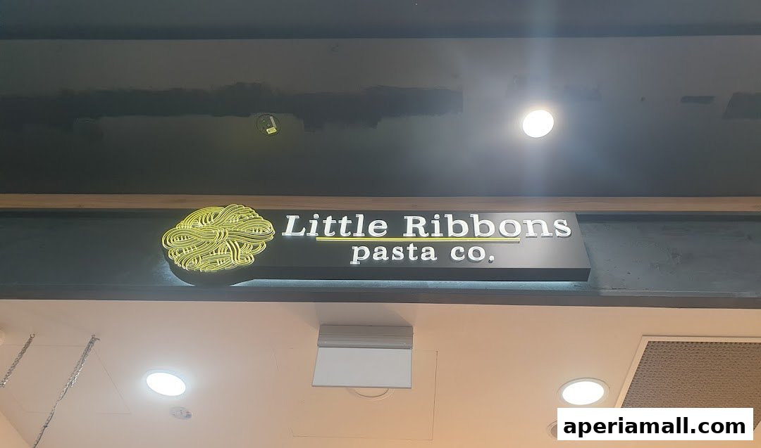 The illuminated sign for Little Ribbons Pasta Co. features a stylized pasta graphic and white lettering.