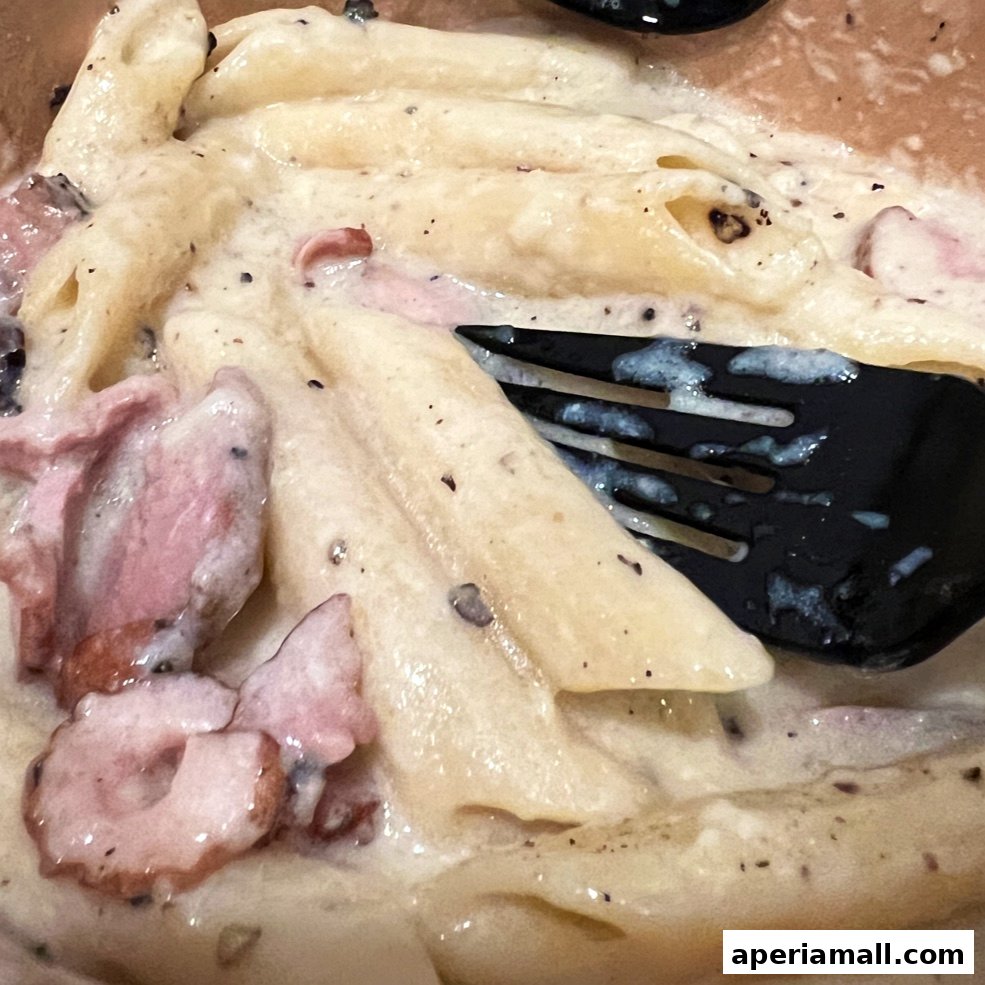 A close-up of creamy pasta with pieces of meat and a fork.