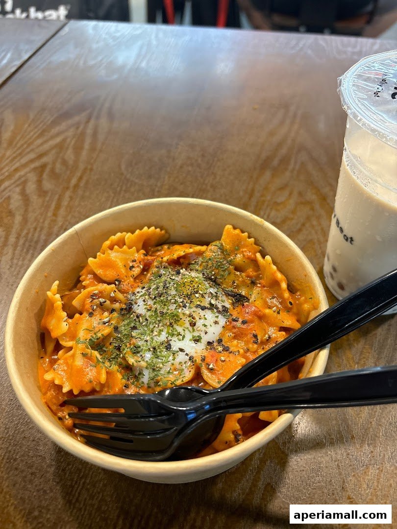 A bowl of farfalle pasta with creamy tomato sauce and a poached egg, served with a drink.