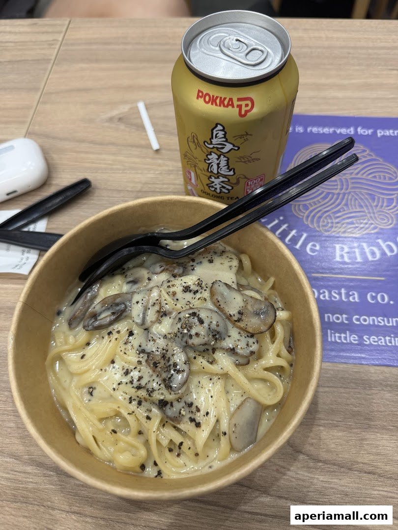 A bowl of creamy mushroom pasta with a can of Oolong tea and cutlery.