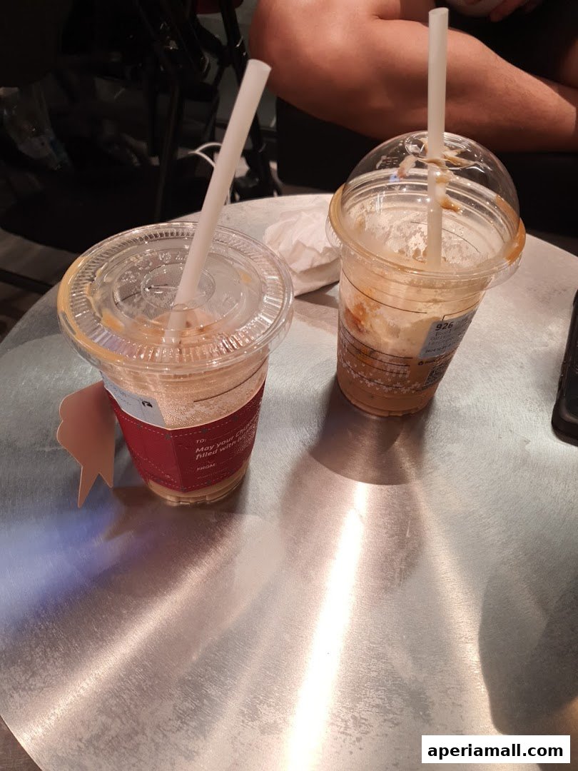 Two iced coffee drinks with straws on a metallic table.