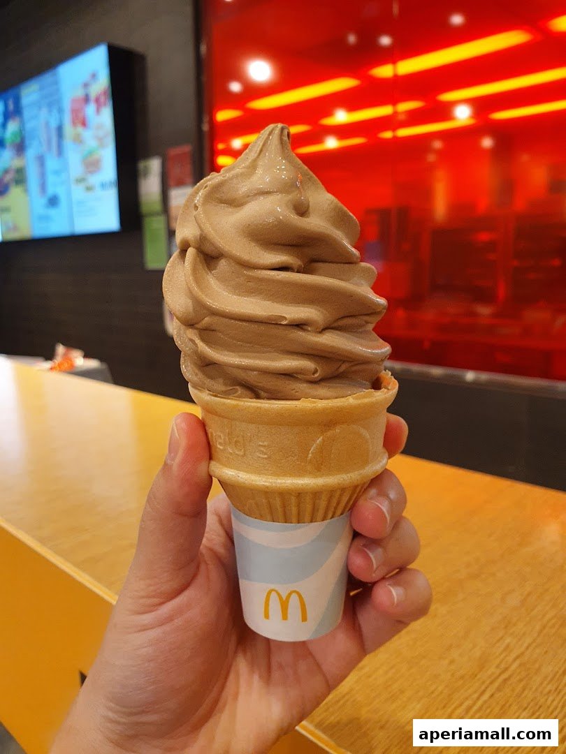 A hand holds a chocolate soft serve ice cream cone from McDonald's.