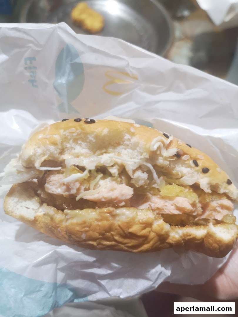 A close-up of a salmon burger with sesame seeds on the bun, partially unwrapped.