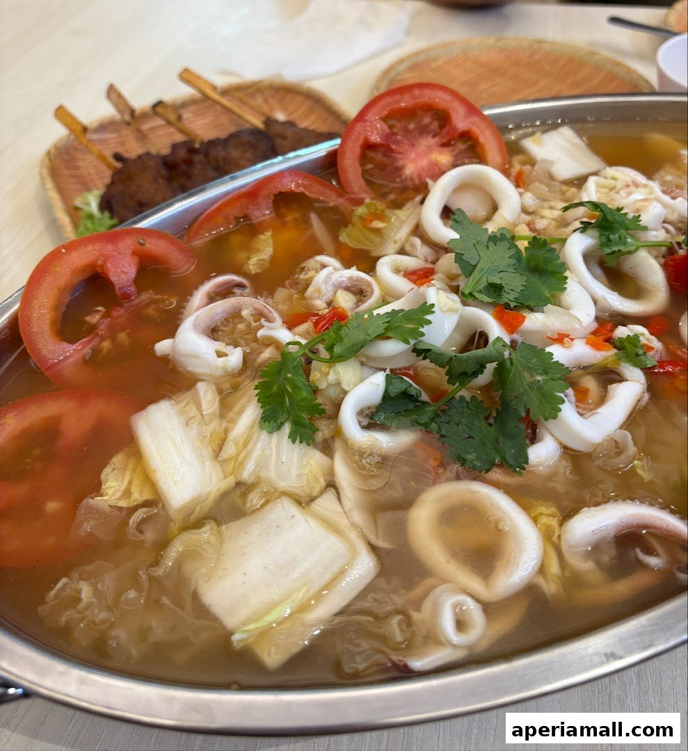 A close-up of a steaming Thai seafood soup with squid, tomatoes, and vegetables.