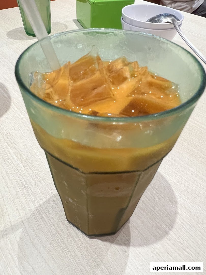 A close-up of a refreshing Thai iced tea with ice in a green glass.