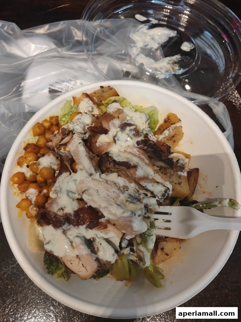 A healthy salad bowl with grilled chicken, chickpeas, broccoli, and potatoes, drizzled with sauce.