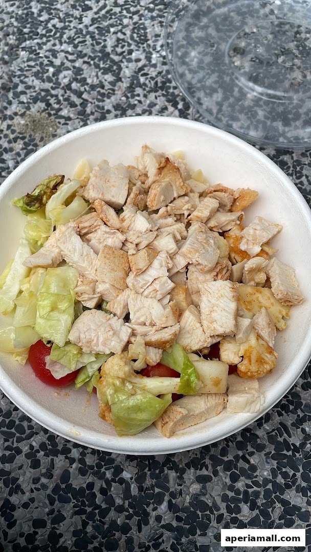 A close-up of a healthy salad with chopped chicken, lettuce, tomatoes, and cauliflower.