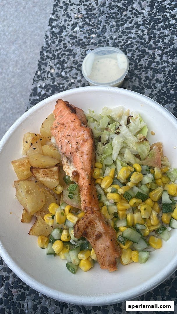 A healthy meal with grilled salmon, roasted potatoes, corn, cucumber salad, and a side of dressing.