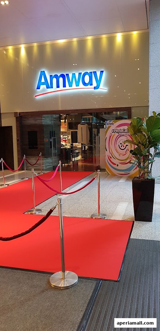 The Amway store entrance is decorated with a red carpet and velvet ropes, with a colorful promotional banner.