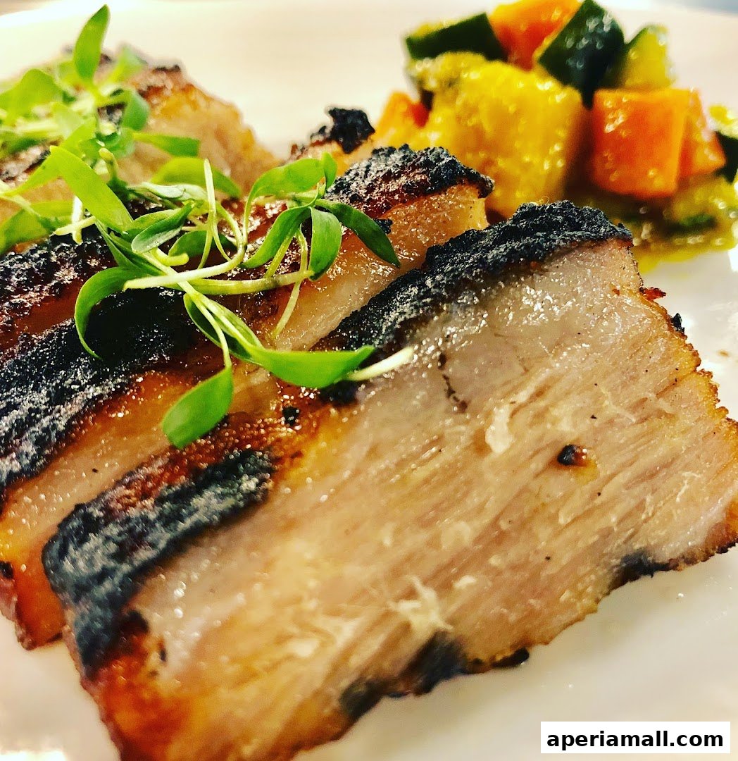 Close-up of perfectly cooked pork belly with crispy skin and a side of roasted vegetables.