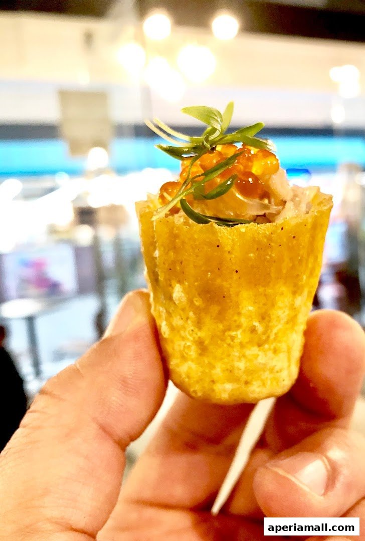 A hand holds a small, golden pastry cup filled with salmon and topped with roe and microgreens.