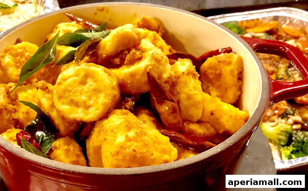 A close-up of a red pot filled with golden-brown fried paneer cubes, garnished with curry leaves and dried chilies.