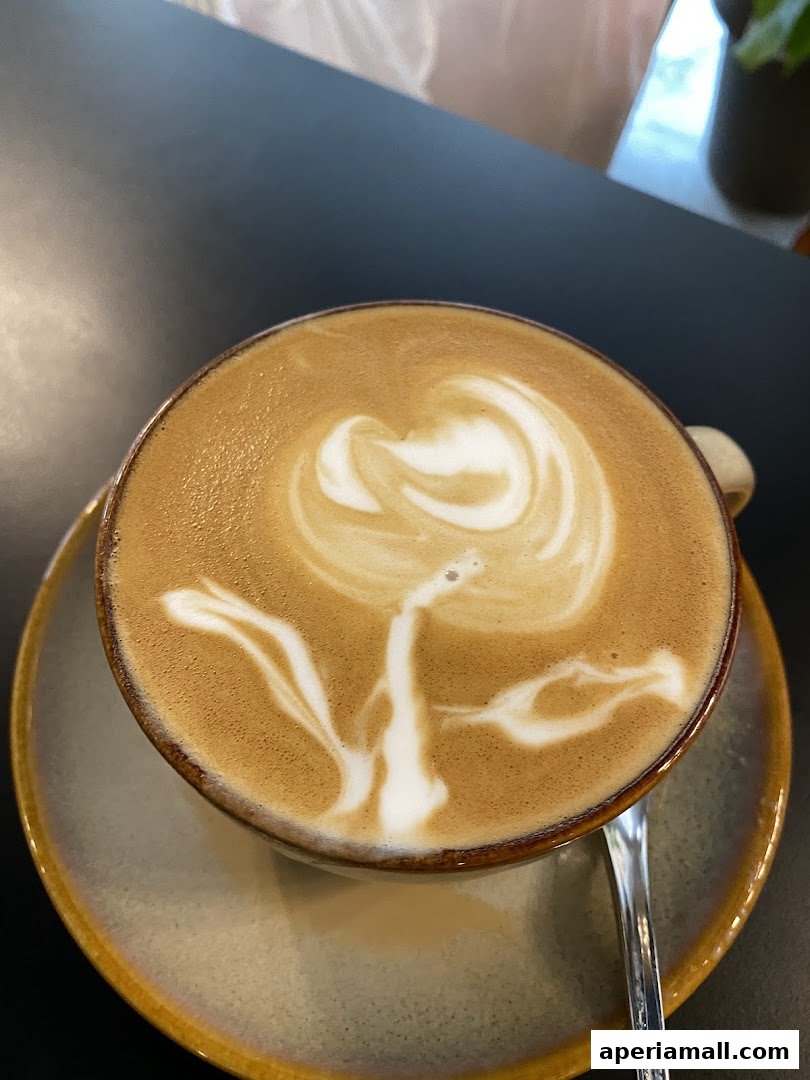 A close-up of a latte with intricate foam art, served in a ceramic cup and saucer.