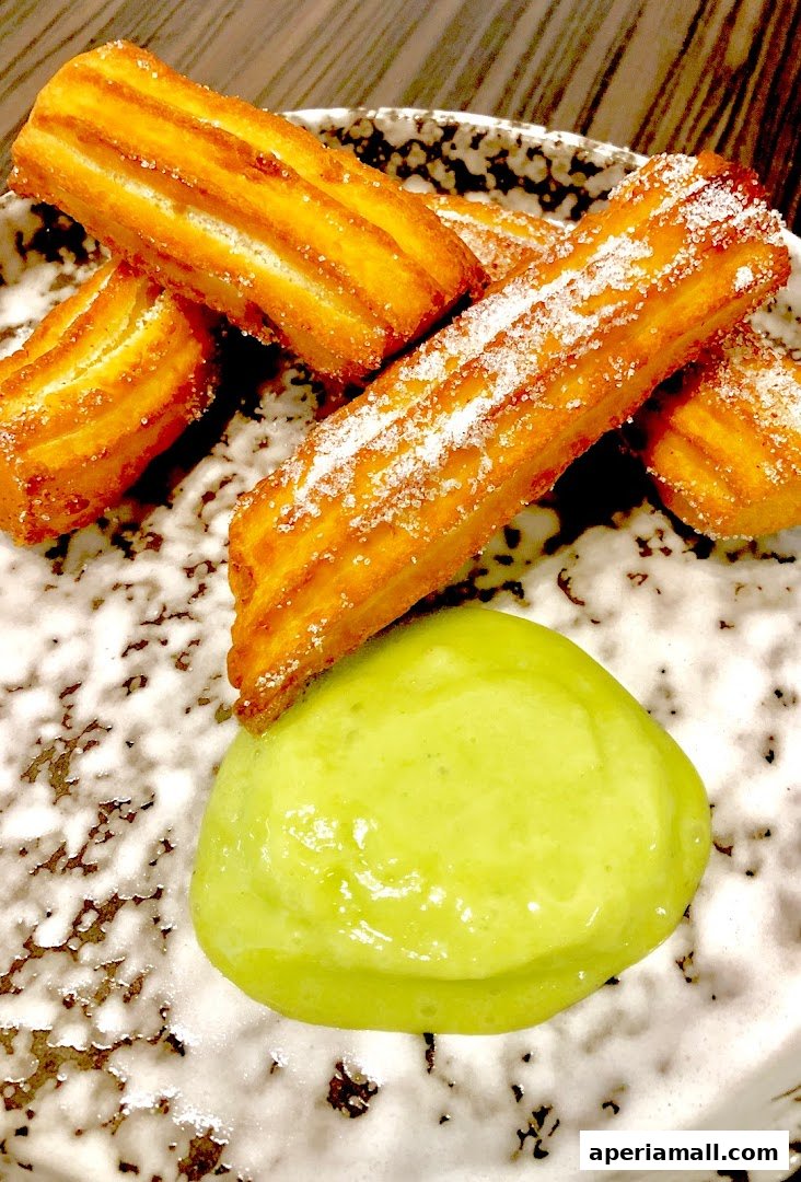 Golden brown churros dusted with sugar served with a vibrant green dipping sauce.