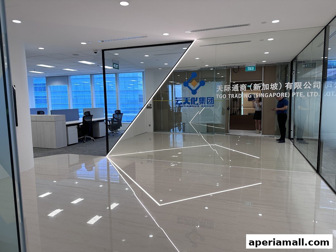 Modern office interior with glass partitions, desks, and a company logo visible.