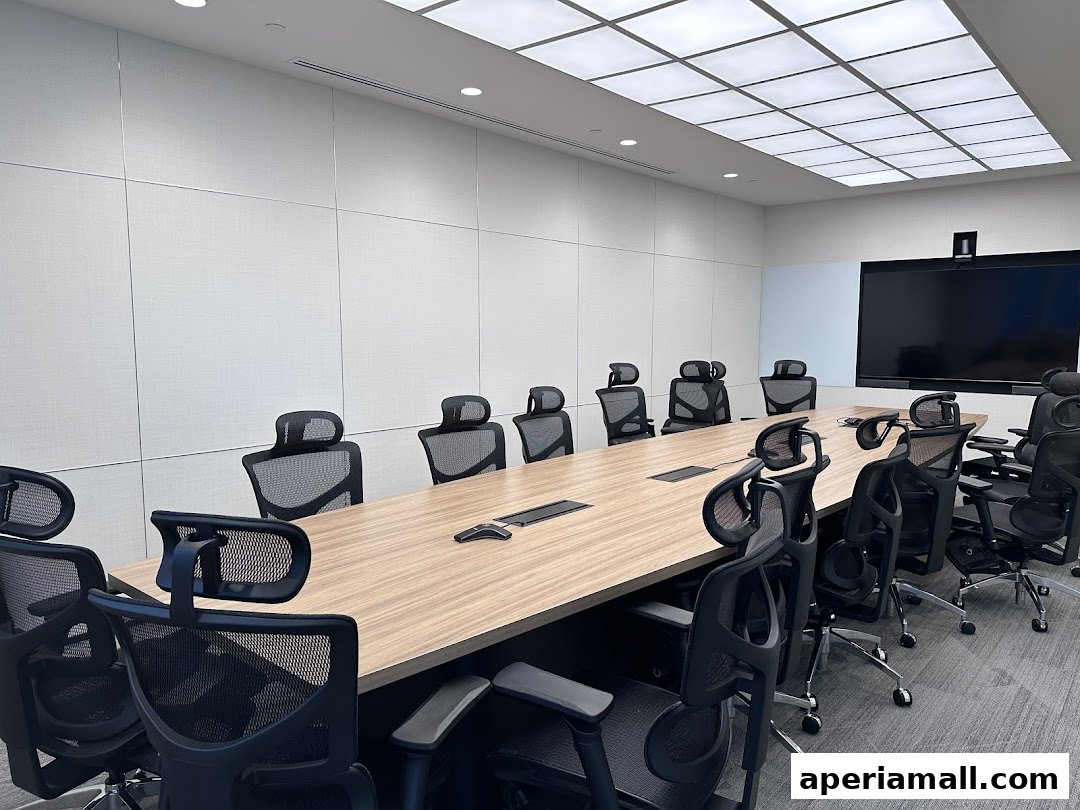 A modern conference room with a long wooden table, ergonomic chairs, and a large screen.