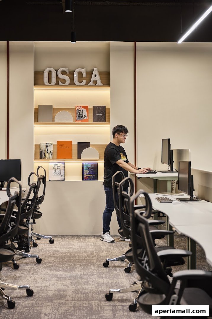 A man stands at a desk in a modern office space with shelves displaying books and decor.