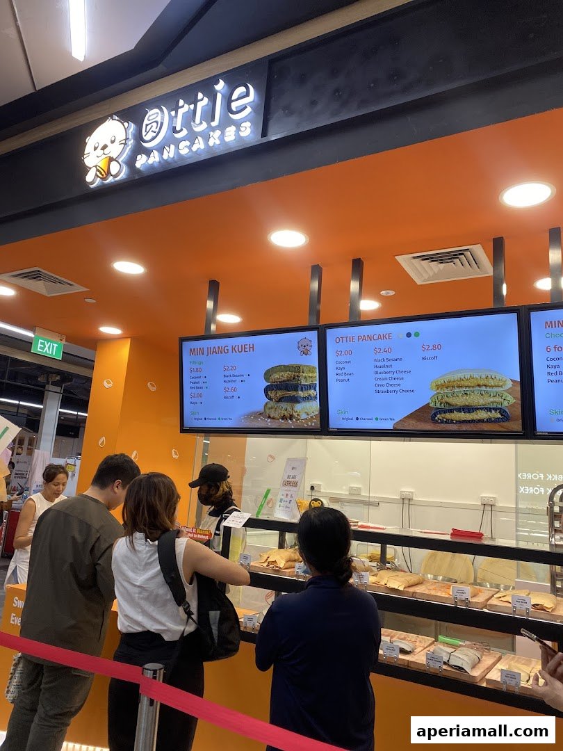 Customers ordering at Ottie Pancakes, a shop with a bright orange interior and digital menus displaying pancake options.