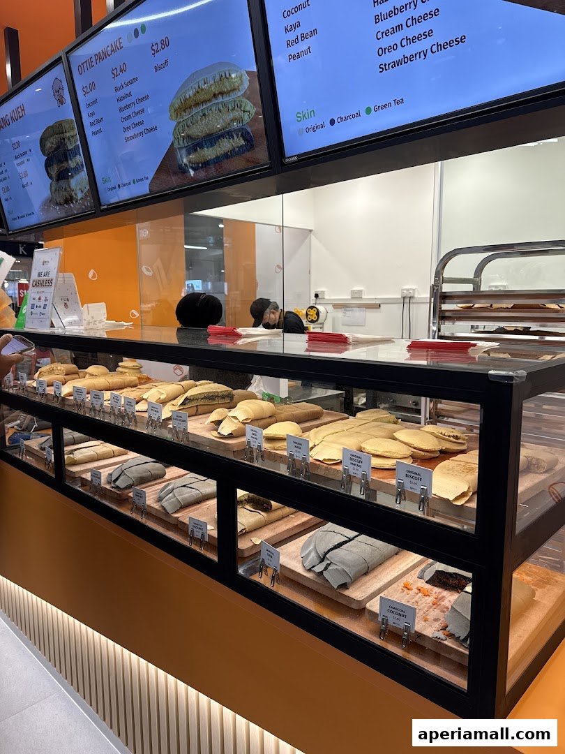A display case filled with various Ottie Pancakes, with a menu board above showing flavors and prices.