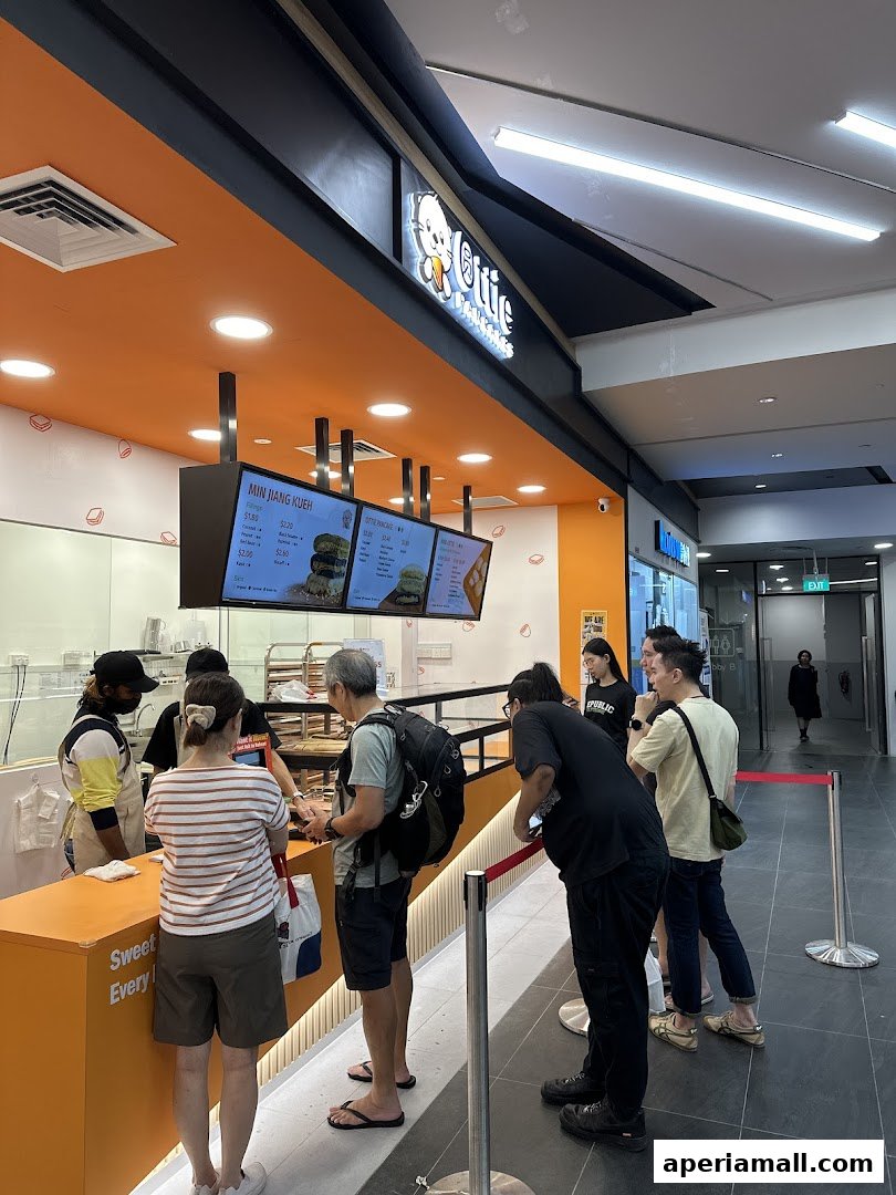 Customers queue at Ottie Pancakes, a shop with an orange counter and menu screens.