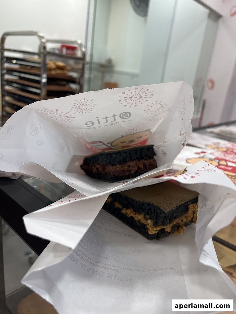 Two charcoal pancakes with different fillings, presented in branded paper bags.