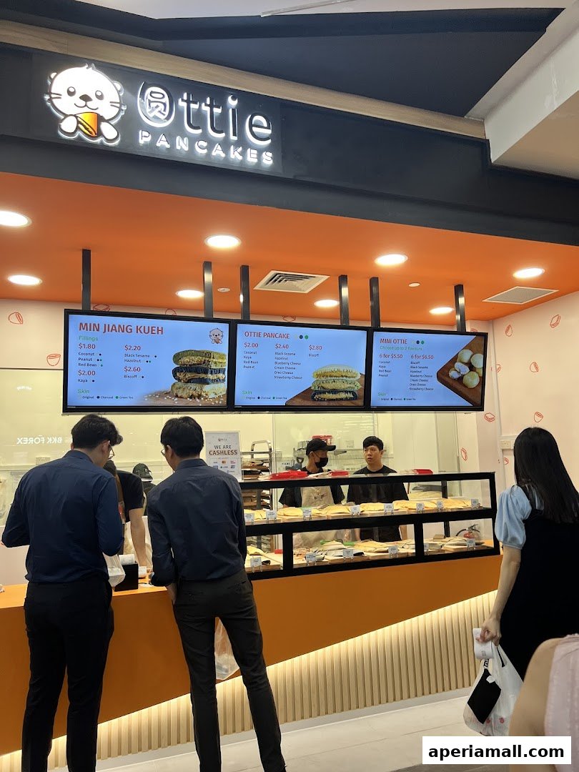 Customers ordering at Ottie Pancakes, a shop with digital menus displaying pancake options.