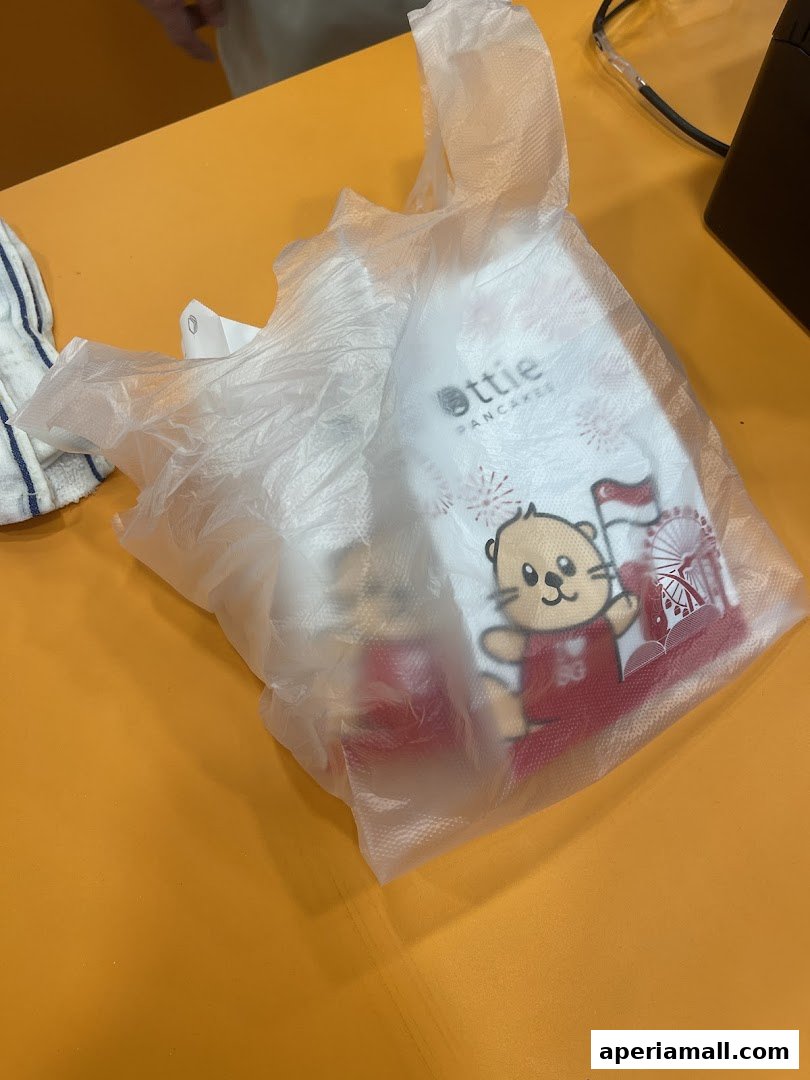 A plastic bag with the Ottie Pancakes logo and a cartoon otter holding a Singapore flag.