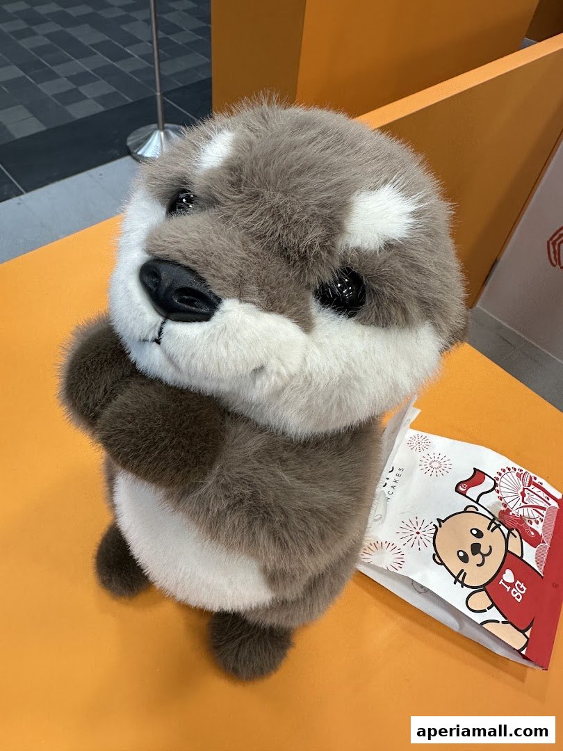 A cute otter plush toy sits next to a branded paper bag with fireworks and an otter graphic.