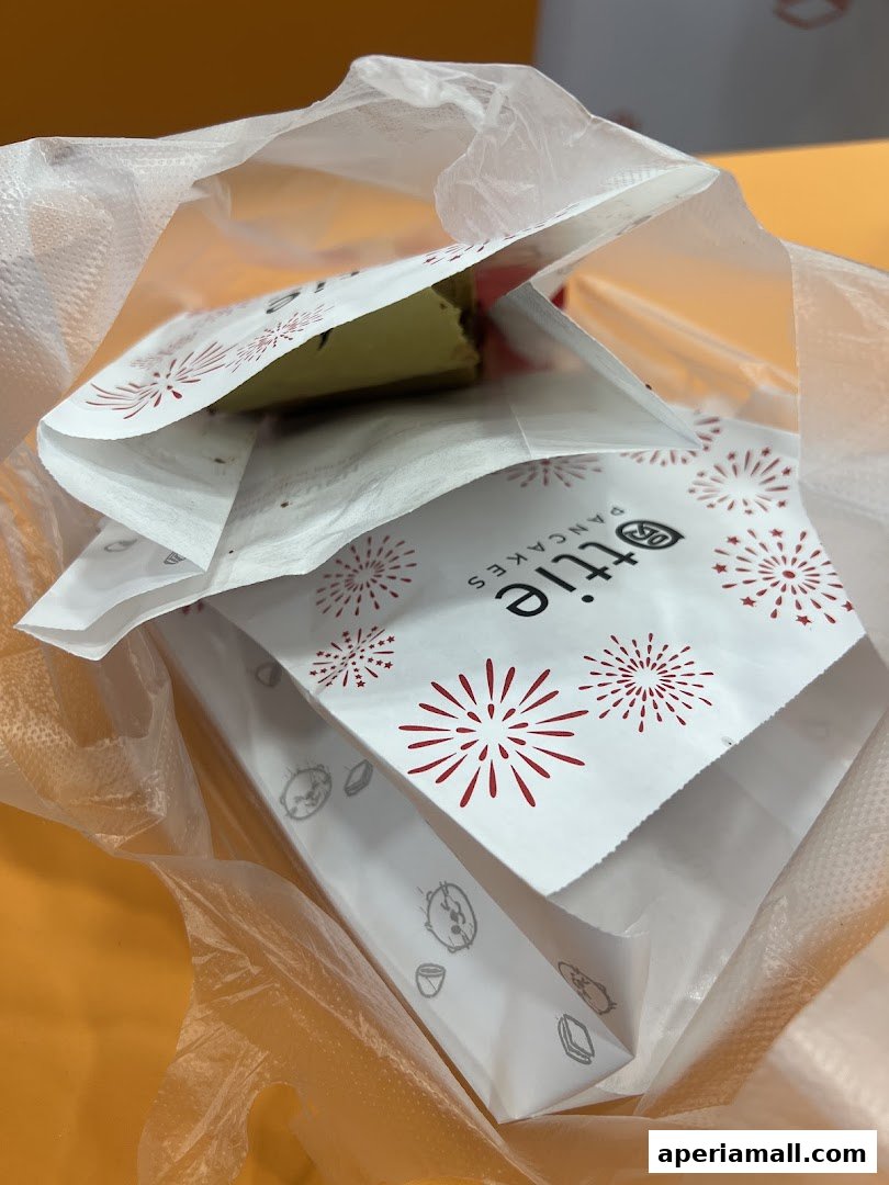 A close-up view of a white paper bag with red firework designs, containing a slice of green dessert.