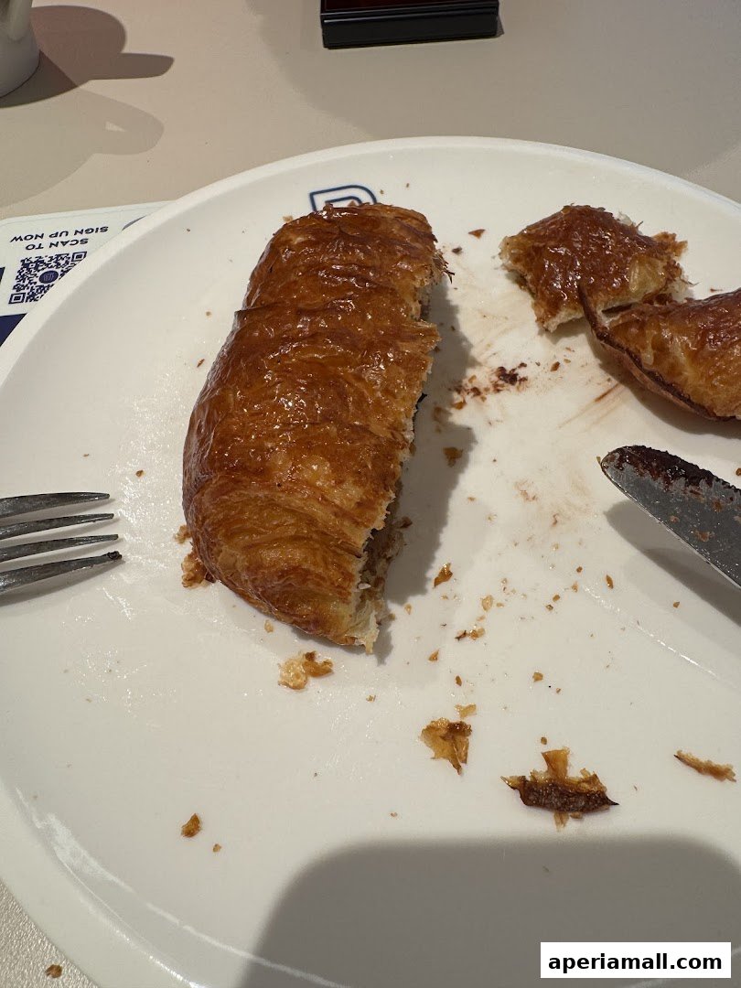 A partially eaten chocolate croissant on a white plate with a fork and knife.