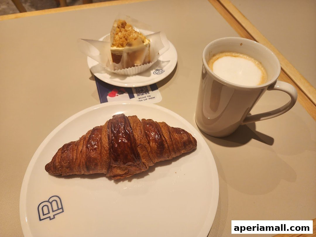 A croissant, a slice of cake, and a latte on a table.
