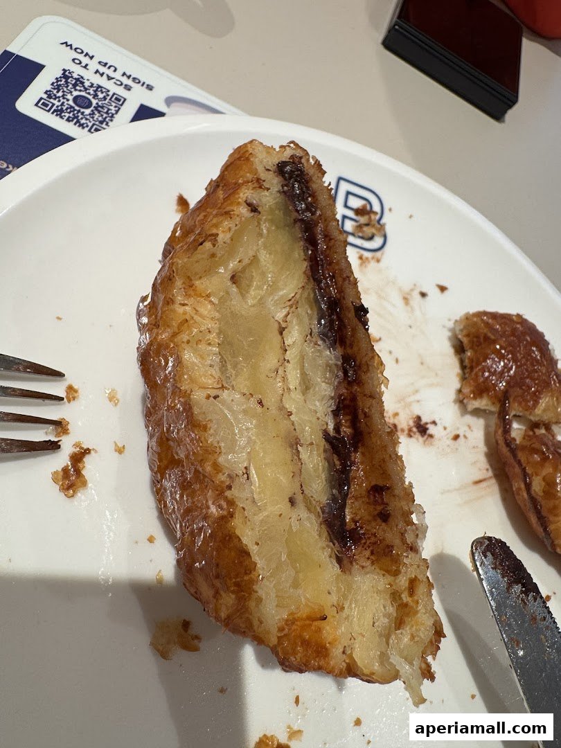 A close-up of a flaky chocolate croissant on a white plate with a fork and knife.