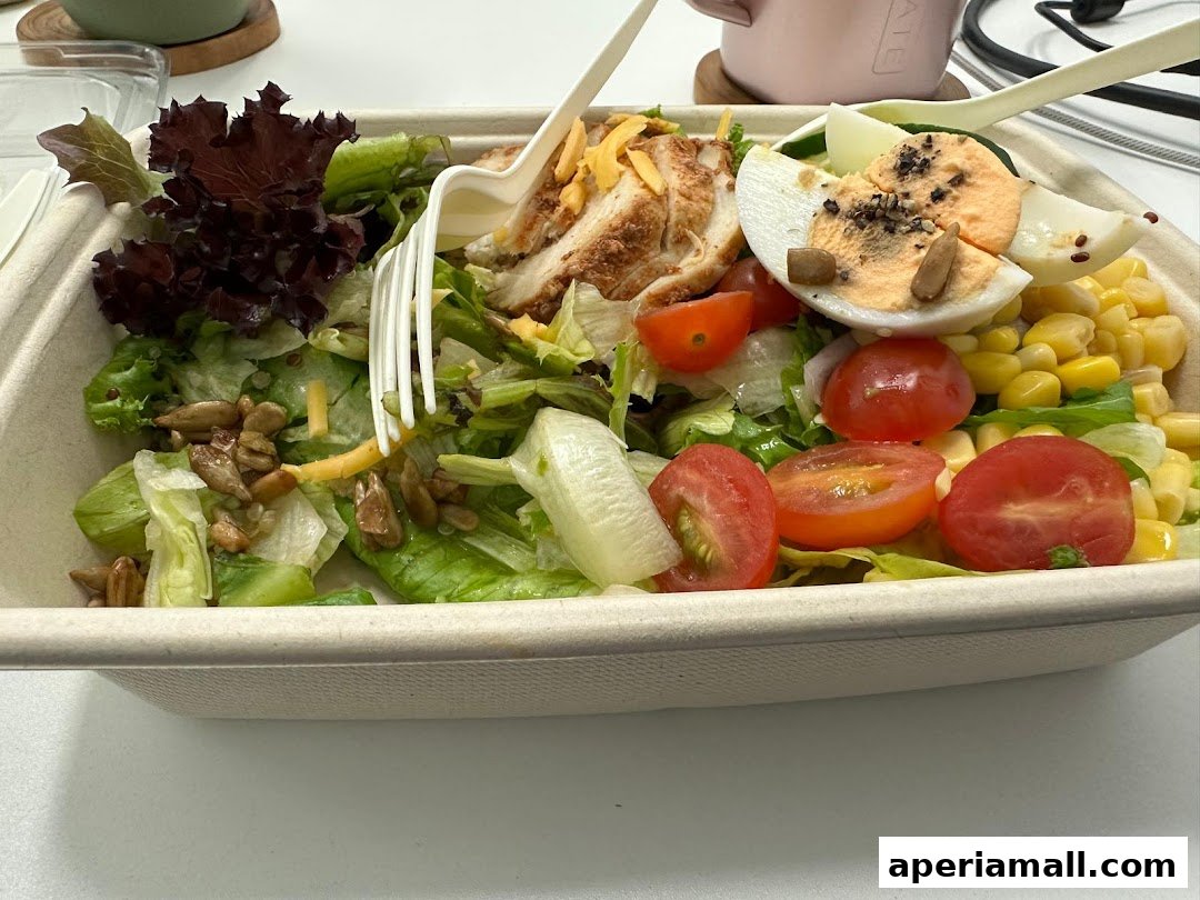 A close-up of a fresh salad in a takeaway container with grilled chicken and boiled egg.