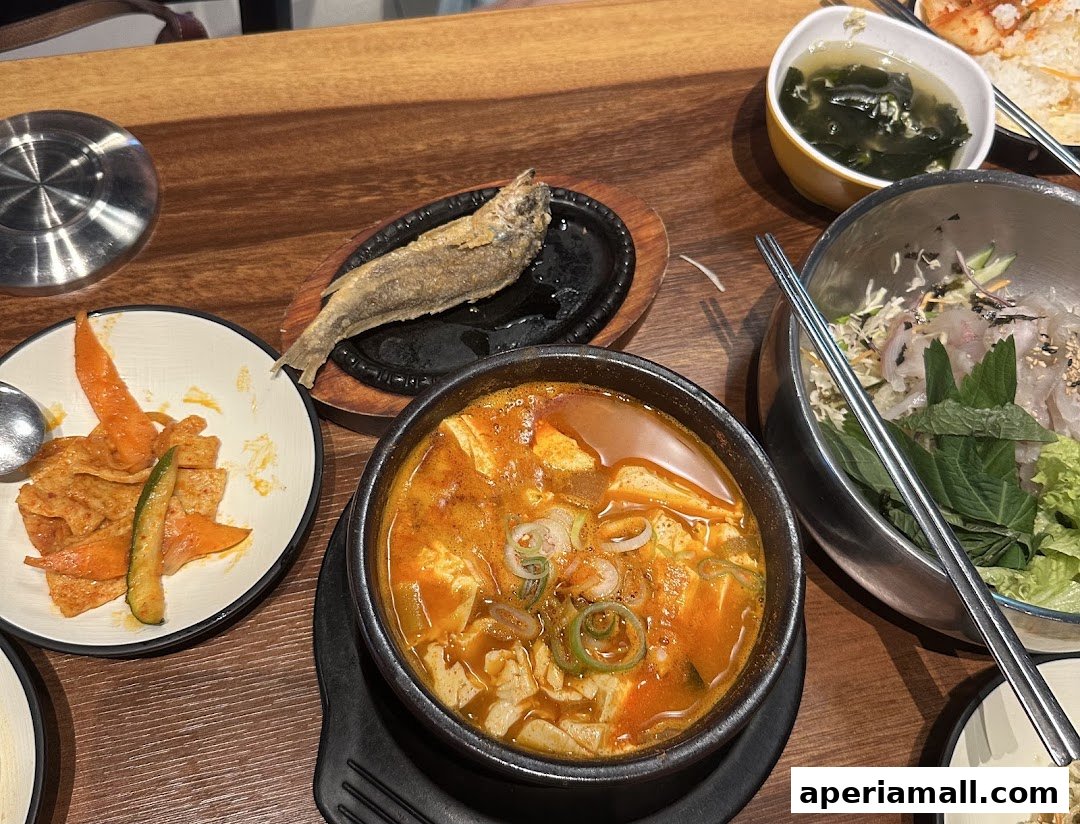 A table laden with Korean dishes including a hearty stew, fried fish, and a fresh seafood salad.