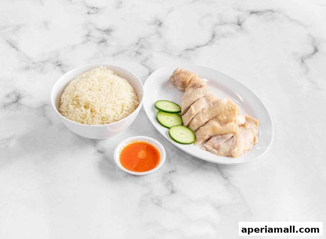 A plate of sliced chicken rice with cucumber slices and a small bowl of chili sauce.