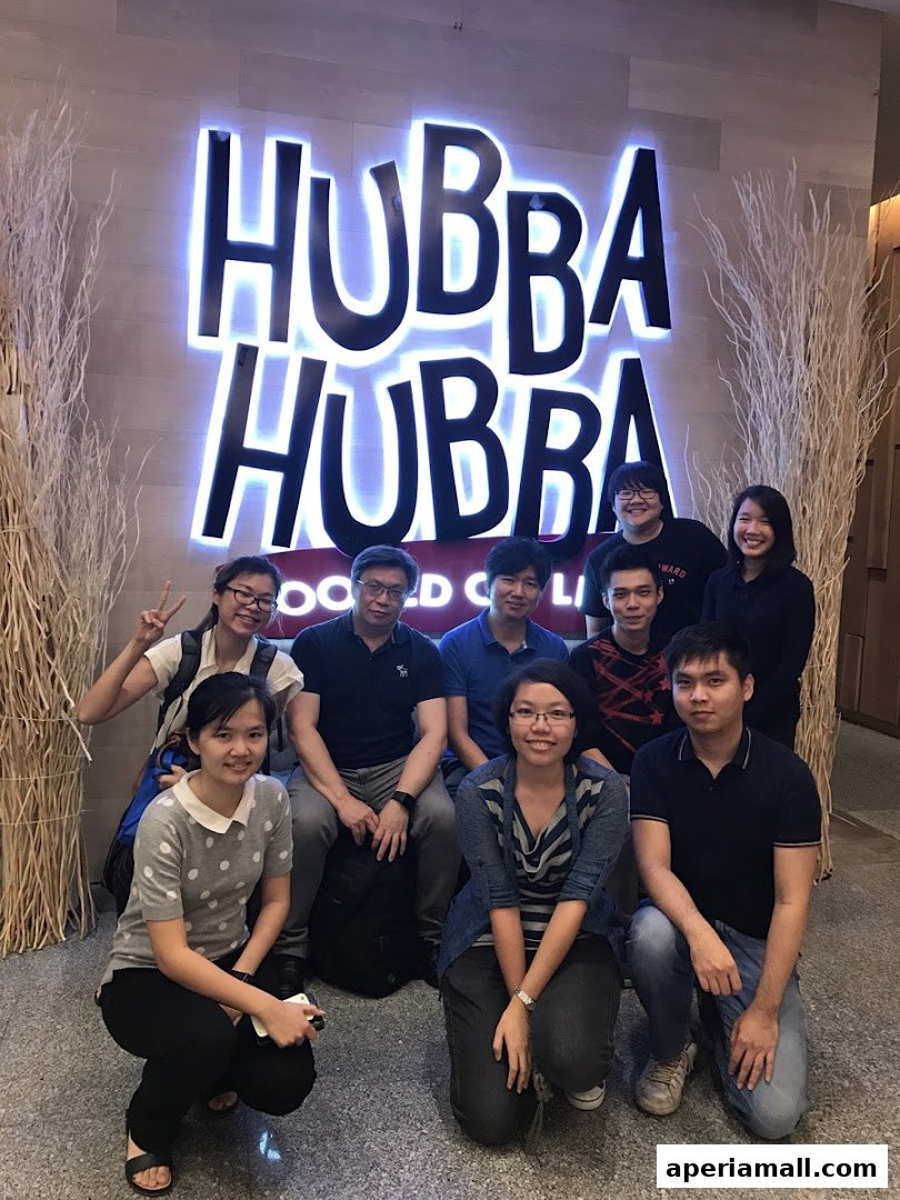 A group of people posing in front of a large illuminated sign that says Hubba Hubba.