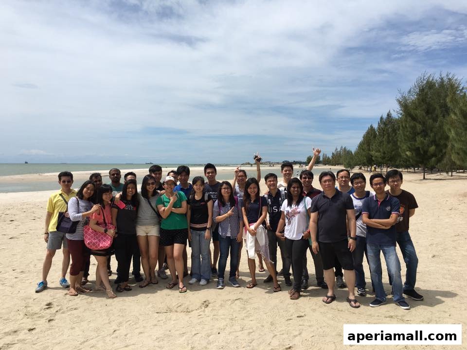 A group of people posing for a photo on a sandy beach with trees and the ocean in the background.