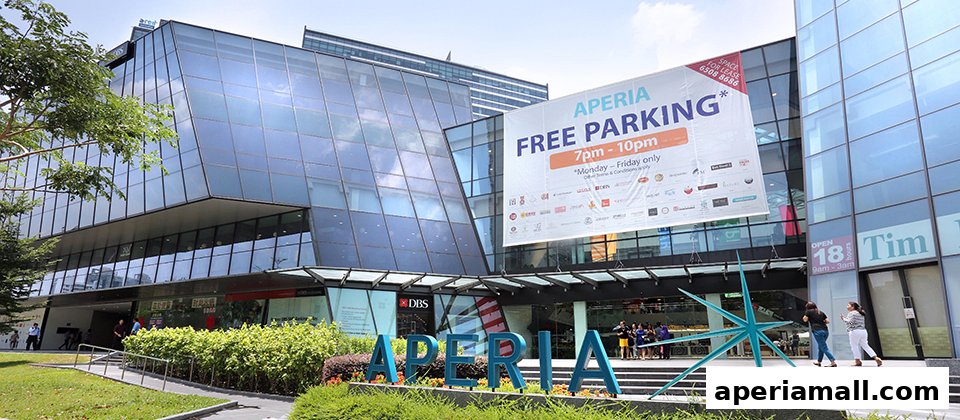 Modern glass building with a large banner advertising free parking and the name APERIA.