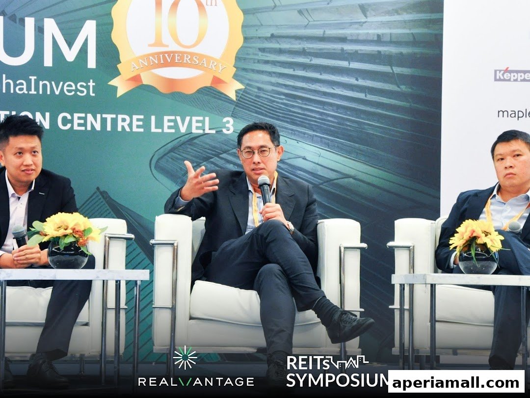 Three men in suits sit on chairs at a panel discussion, with a banner behind them.