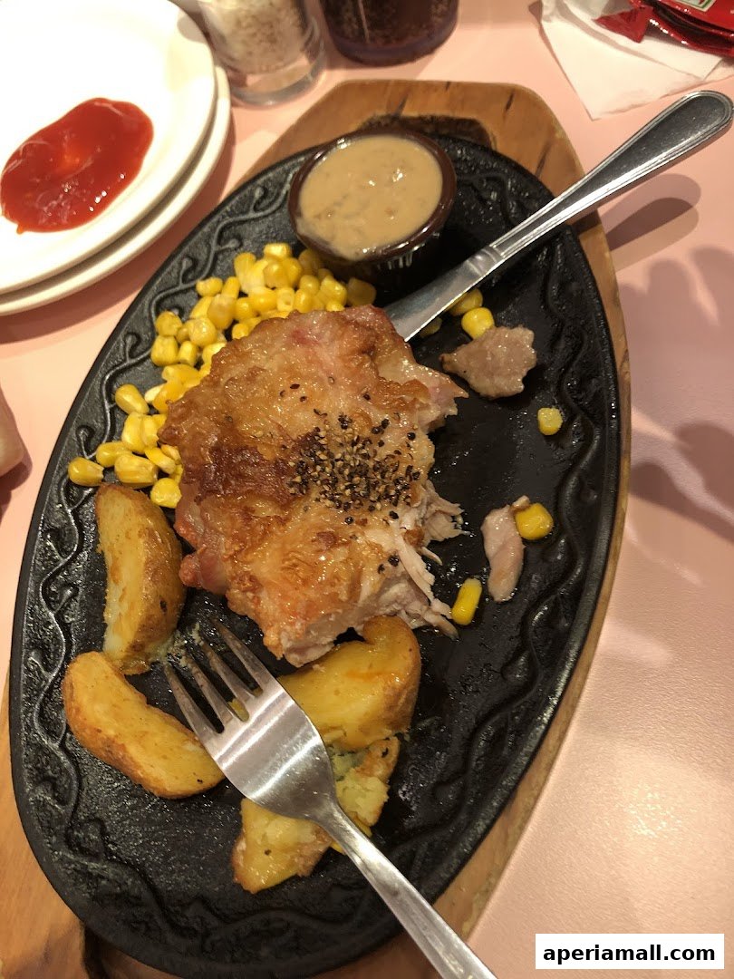 A sizzling hot plate of chicken, corn, and potato wedges with a side of sauce.