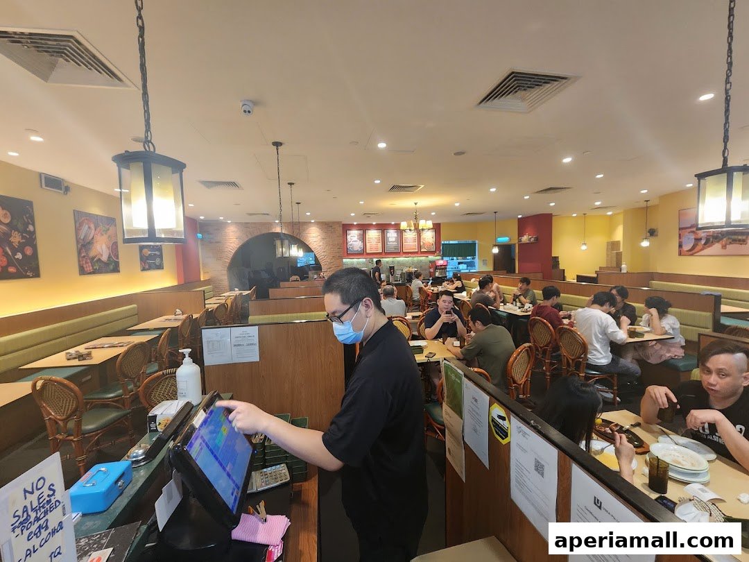 A server operates a POS system in a busy Saizeriya restaurant with diners seated at tables.