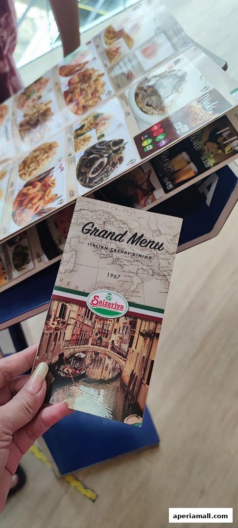 A hand holds a Saizeriya Grand Menu featuring Italian casual dining and Venice imagery.