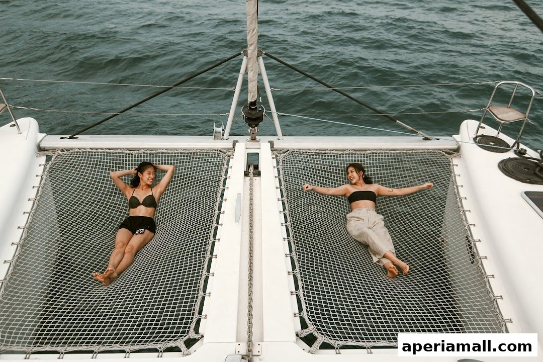 Two women relax on the netting of a catamaran sailing on the ocean.
