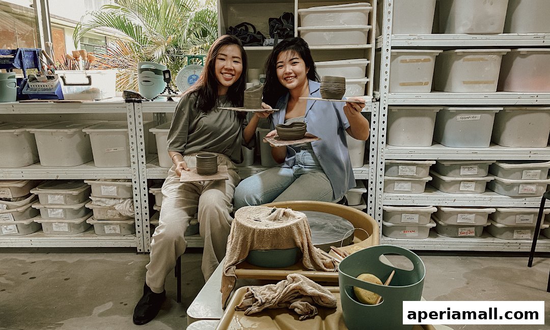 Two smiling women proudly display their handmade pottery creations in a studio setting.