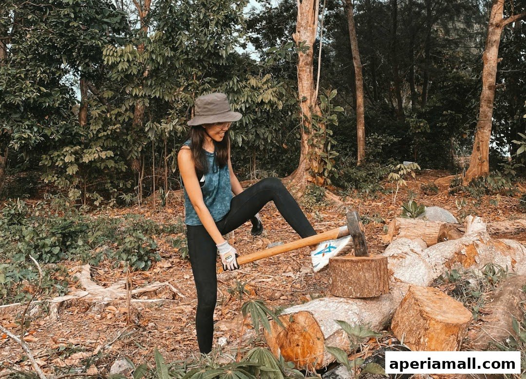 A woman in a hat and athletic wear chops wood in a forest setting.