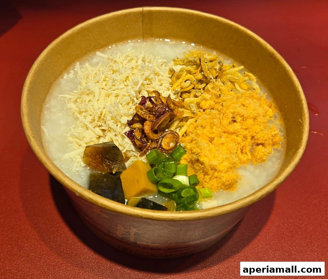 A bowl of savory congee topped with shredded chicken, dried fish, fried shallots, and scallions.
