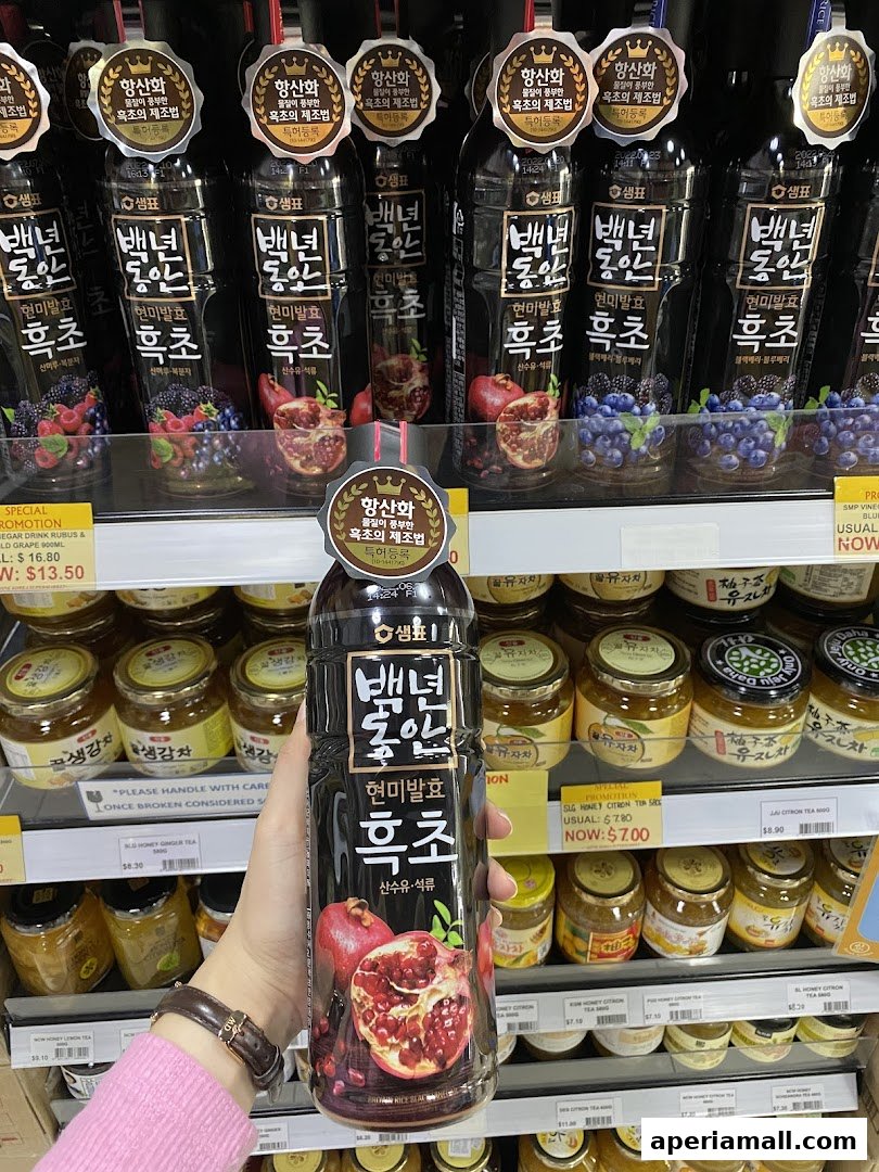 A hand holds a bottle of Korean black vinegar with pomegranate and berries, displayed in a store.
