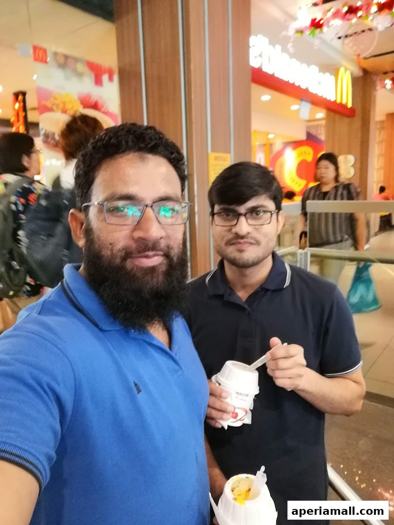 Two men are smiling and holding ice cream cups in front of a McDonald's restaurant.
