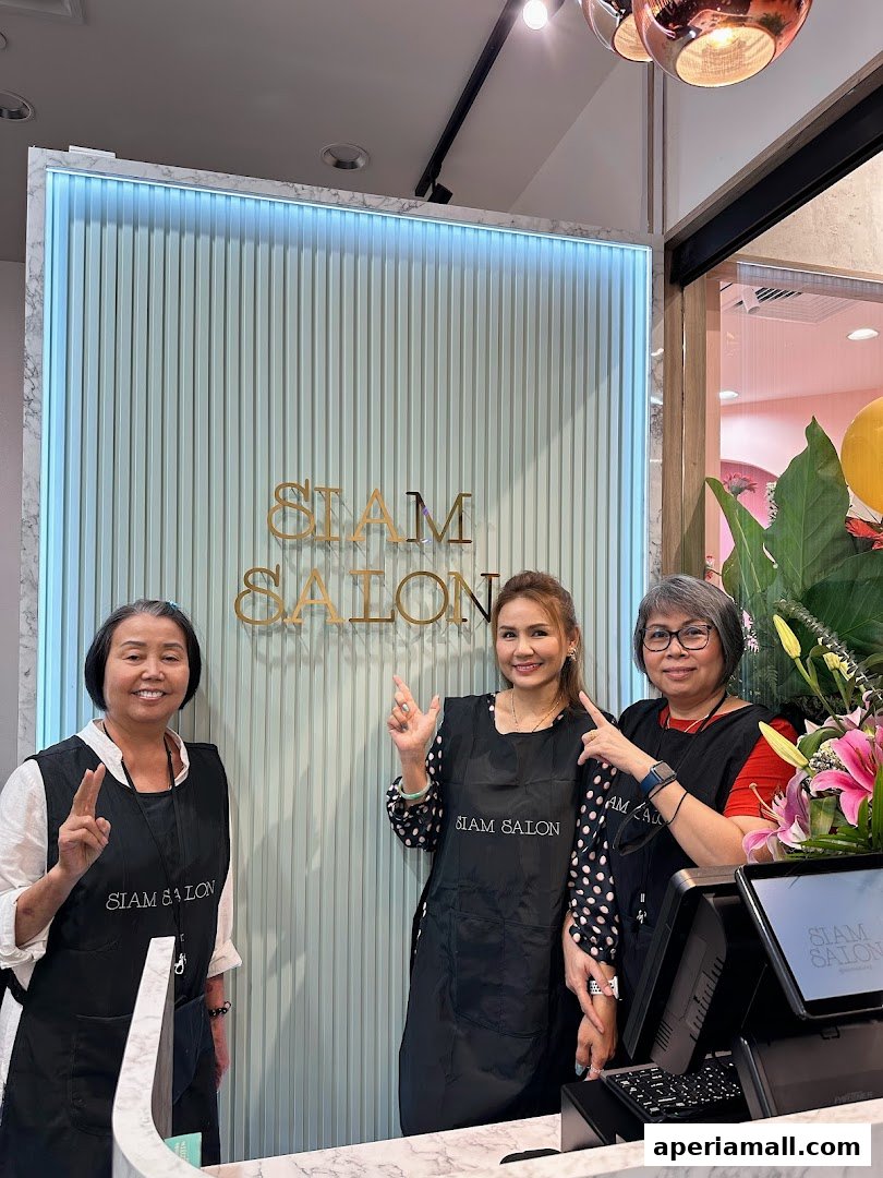 Three smiling women in aprons stand in front of a salon with the name 'Siam Salon' displayed.