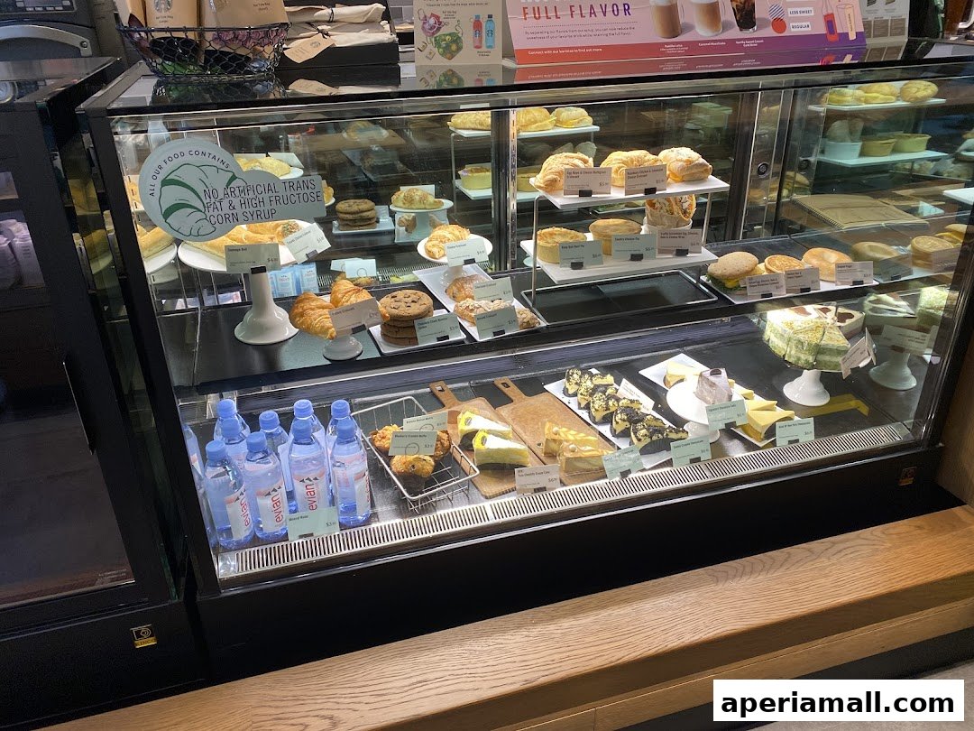 A display case filled with various pastries, cakes, sandwiches, and bottled water.